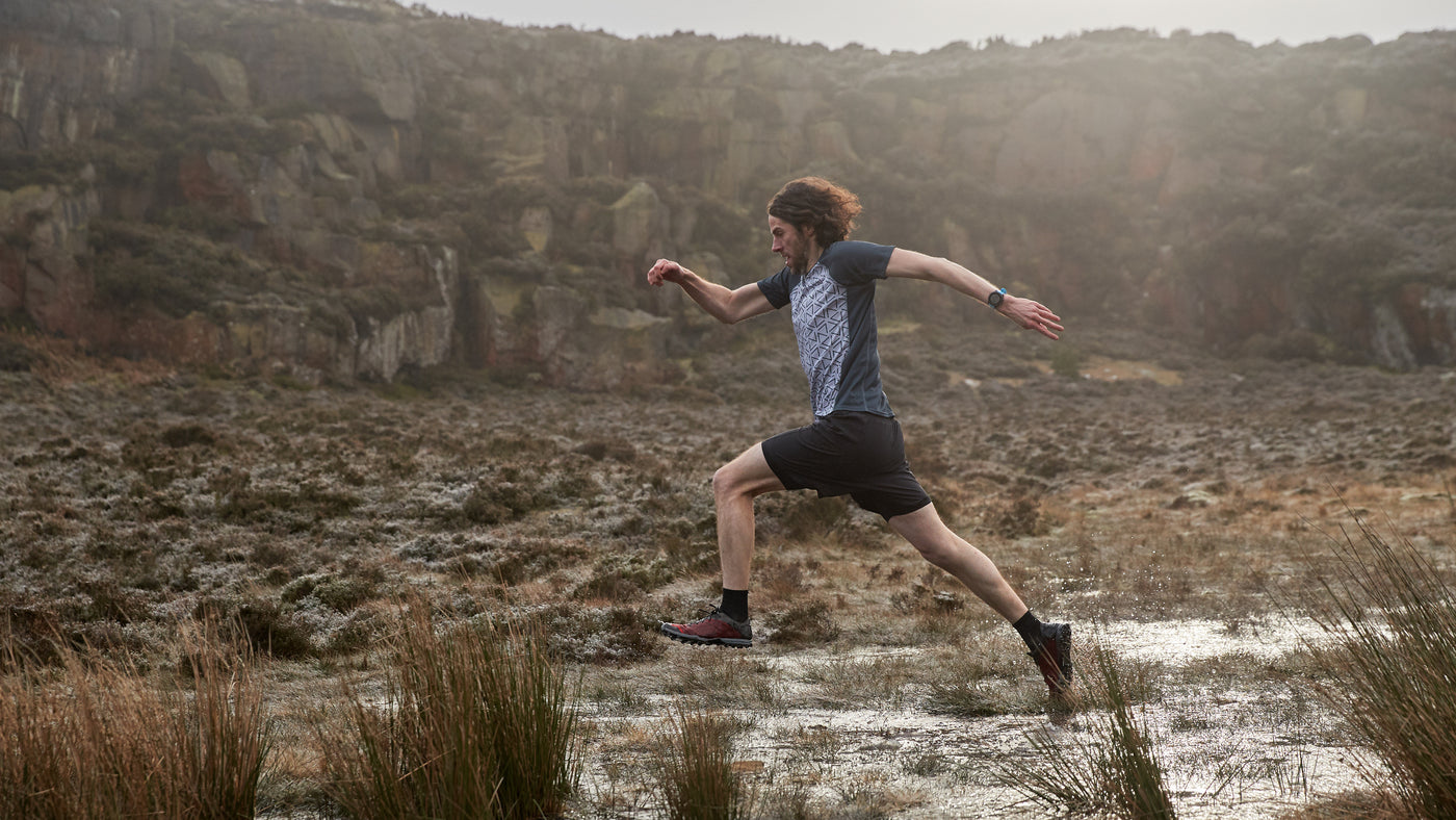 Runner jumping over puddle on a trail wearing a recycled running t-shirt